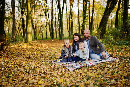 Happy caucasian family of mom dad and little girl with boy sitting on plaid at majestic autumn fall forest. © AS Photo Family