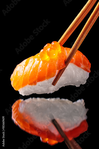 Salmon sushi nigiri in chopsticks isolated on black background with reflection.Close up.
