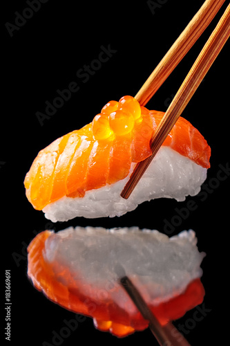 Salmon sushi nigiri in chopsticks isolated on black background with reflection.Close up.