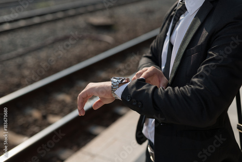 Businessman looking at the time on his wrist watch at train station background.