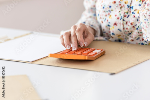 Woman calculating on orange desktop calculator photo