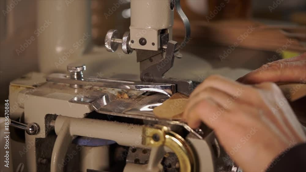 close up shot of a man's hands, who works on industrial weaving equipment, in his workshop he uses a machine to frame the edge of a leather piece of material close up shot of a man's hands, who works on industrial weaving equipment, in his workshop he uses a machine to frame the edge of a leather piece of material
