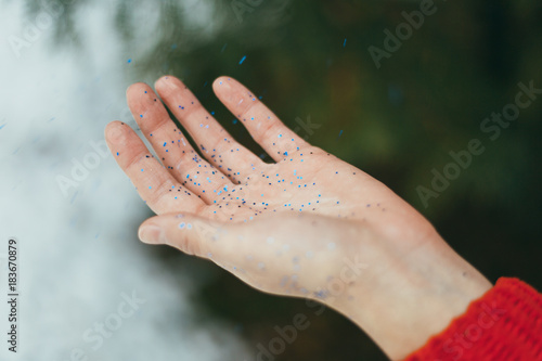Young beautiful girl holding on hands blue glitters on green background.
