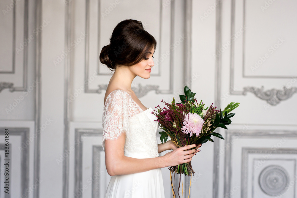 Bride in white dress sitting on chair indoors in dark studio interior like at home.