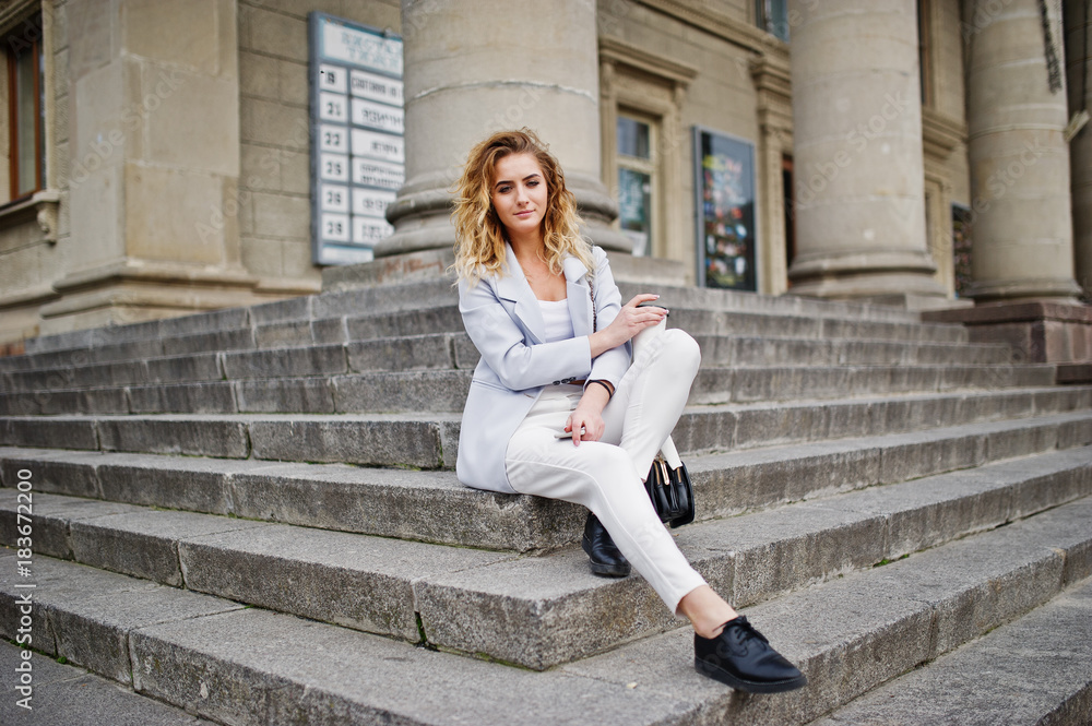Stylish curly blonde model girl wear on white with cup of coffee posing on stairs outdoor. Stylish curly blonde model girl wear on white with cup of coffee posing on stairs outdoor.
