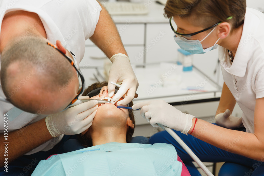 Process of preparing and installing dental ceramic crown. Male professional dentist and female assistant helps to treat the teeth of woman patient in clinic light office with modern tools equipment. Process of preparing and installing dental ceramic crown. Male professional dentist and female assistant helps to treat the teeth of woman patient in clinic light office with modern tools equipment.