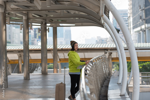 Happy female tourist with suitcase exploring map while standing in city building © xreflex