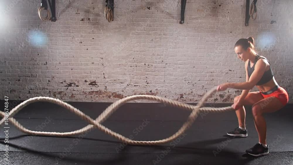 Athletic young woman doing some crossfit exercises with a rope indoor. Slow motion.