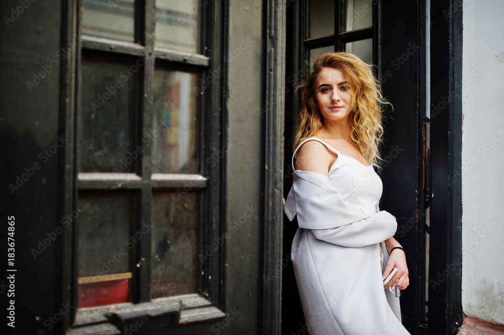 Fototapeta premium Stylish curly blonde model girl wear on white posing against old wooden door.