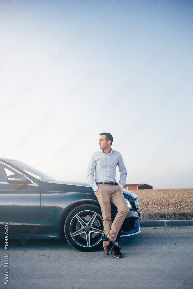 handsome stylish man in leather jacket and sunglasses posing near car at  street Stock Photo by LightFieldStudios