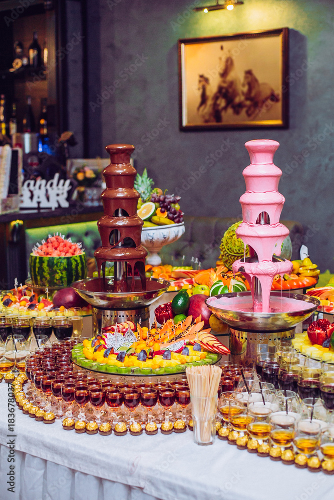 Delicious sweets and fruits on candy buffet. Lot of colorful desserts on table. Chocolate fountain. Party catering.