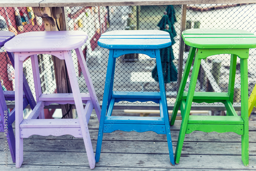 Colorful vivid chairs painted purple, blue and green on waterfront bar restaurant Colorful vivid chairs painted purple, blue and green on waterfront bar restaurant