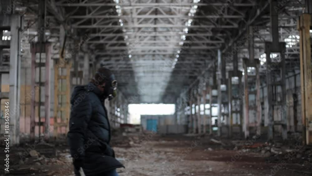 Man in gas mask with wrench as a weapon goes on background of abandoned factory, stalker apocalipse survival concept Man in gas mask with wrench as a weapon goes on background of abandoned factory, stalker apocalipse survival concept