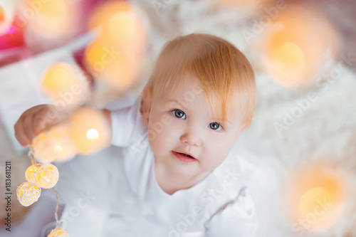 Beautiful little baby celebrates Christmas. New Year's holidays. Sweet baby girl in cute dress having fun in festive decorated room.