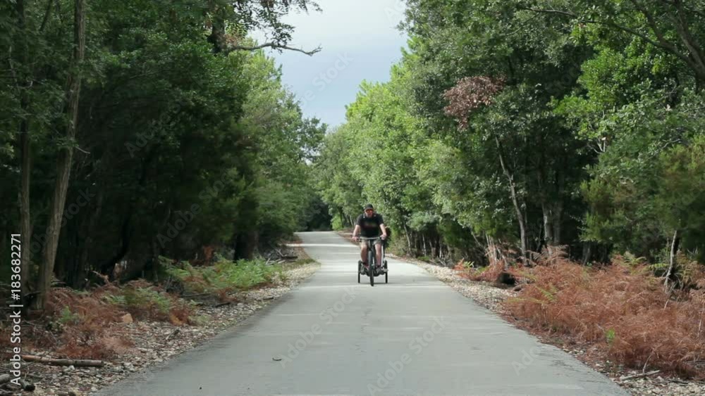 Man riding bicycle with his child in a bicycle trailer in the forest Man riding bicycle with his child in a bicycle trailer in the forest