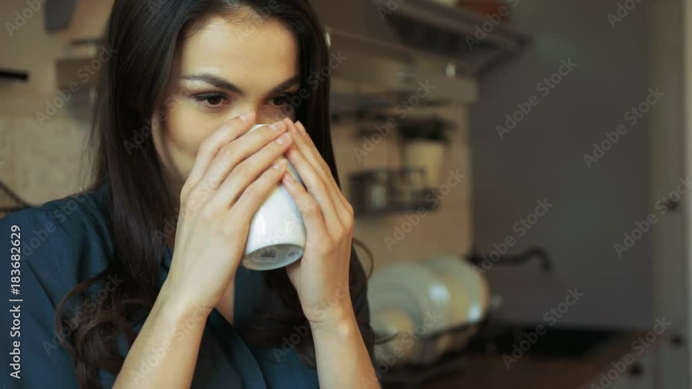 Close up of young beautiful brunette woman drinking hot coffee and smiling in the nice cozy kitchen. Inside. Portrait Close up of young beautiful brunette woman drinking hot coffee and smiling in the nice cozy kitchen. Inside. Portrait