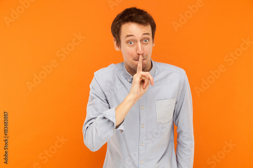 Shh, it's secret! Businessman holding finger near mouth and looking at camera with big shocked eyes.
