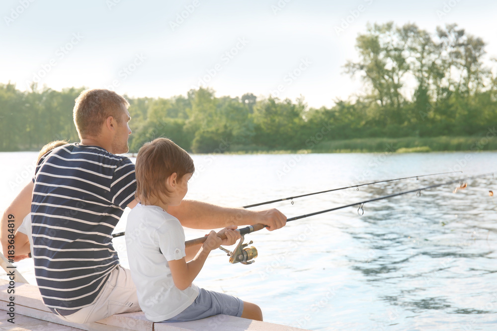 Father with sons fishing from pier on river Father with sons fishing from pier on river
