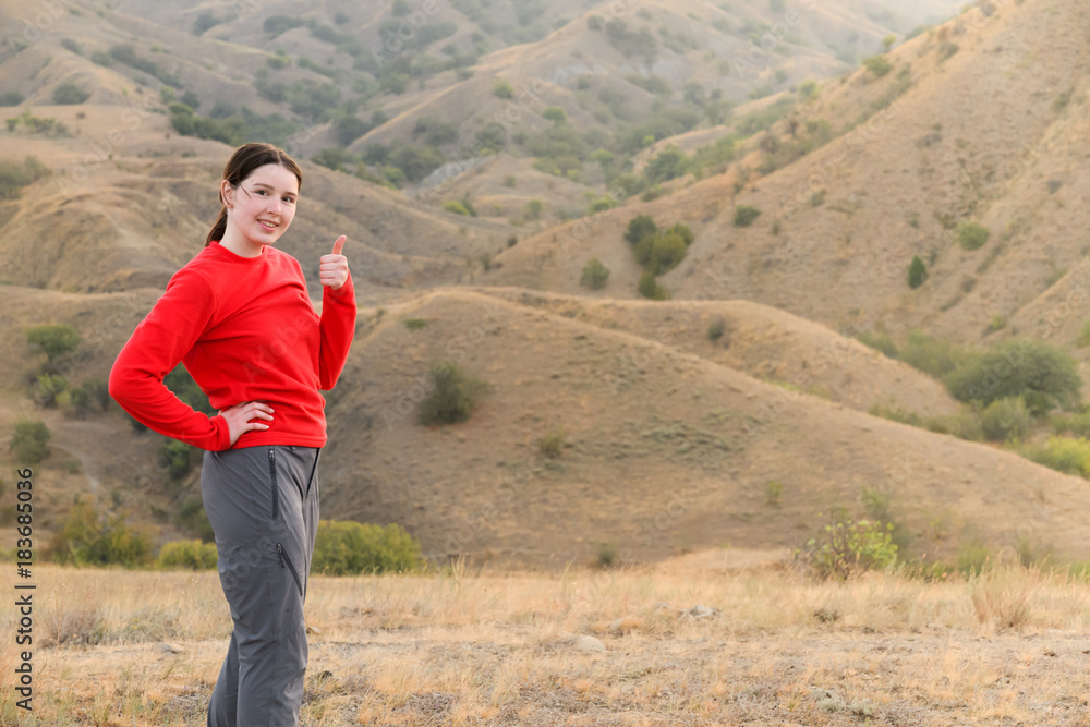 A girl stands and shows sign thumb up tilting the head, in the mountains, steppes