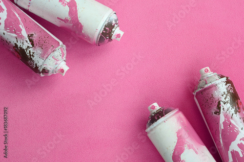 Some used pink aerosol spray cans with paint drips lies on a blanket of soft and furry light pink fleece fabric. Classic female design color. Graffiti hooliganism concept