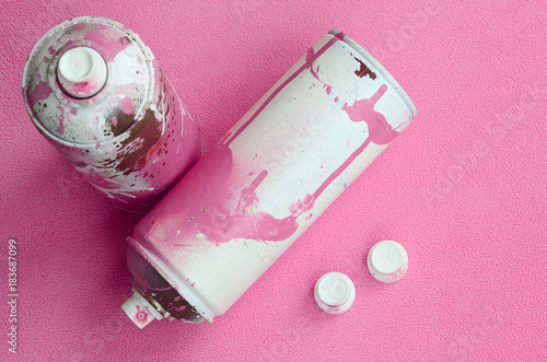Some used pink aerosol spray cans and nozzles with paint drips lies on a blanket of soft and furry light pink fleece fabric. Classic female design color. Graffiti hooliganism concept