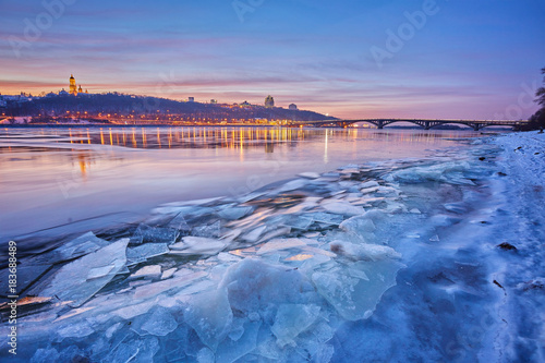 Bridge on the River Dnieper in the evening. Lantern light is reflected in the frozen ice  city