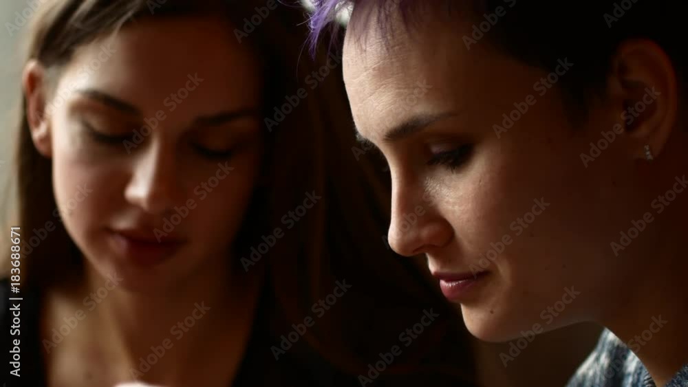 Two friends in a cafe watch video on the smartphone and laugh. Women drink coffee in the coffee house Two friends in a cafe watch video on the smartphone and laugh. Women drink coffee in the coffee house