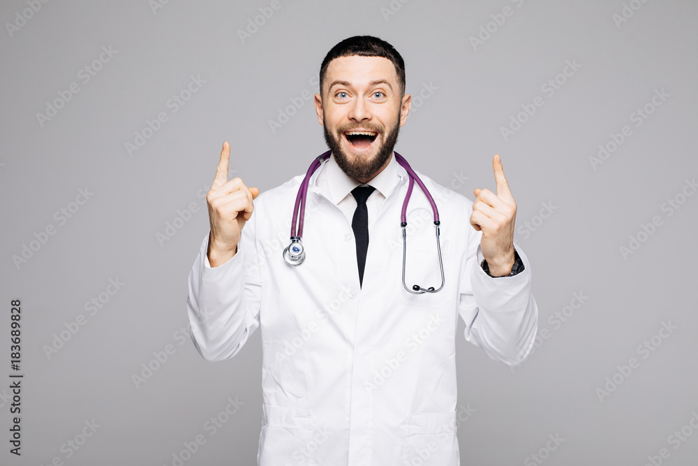 Portrait of a happy excited male doctor dressed in uniform pointing two fingers up and looking at camera isolated over white background Portrait of a happy excited male doctor dressed in uniform pointing two fingers up and looking at camera isolated over white background