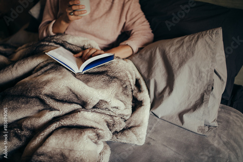 Photos Woman on bed reading book and drinking coffee