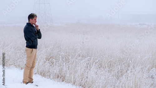 Farmer with sad face, bad mood stands at wheat field covered in snow, winter foggy day. 16x9 wide screen, banner size