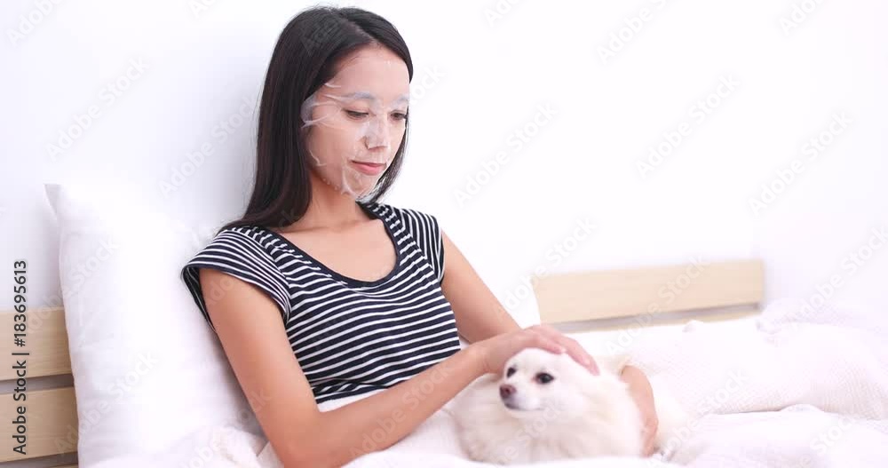 Woman using paper mask and play with her dog on bed Woman using paper mask and play with her dog on bed