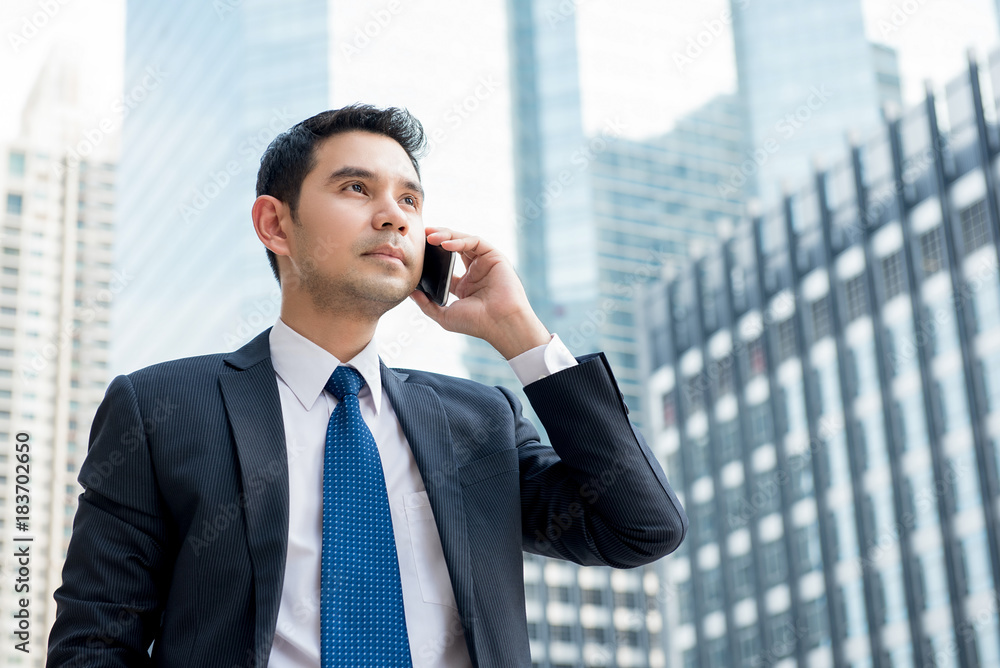 Asian businessman standing outdoors calling on mobile phone in central business district Asian businessman standing outdoors calling on mobile phone in central business district