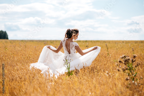 A beautiful bride in wedding dress is dancing alone in a field of wheat. View from the back