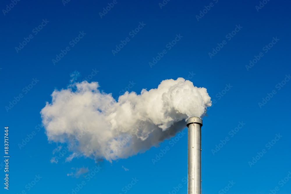 A metallic chimney giving off a heavy cloud of white smoke against a deep blue sky. A metallic chimney giving off a heavy cloud of white smoke against a deep blue sky.