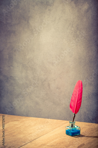 Vintage old red quill pen with inkwell on wooden table front concrete wall background. Retro style filtered photo