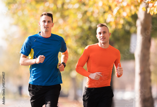 Handsome young men wearing sportswear and running at quay during autumn