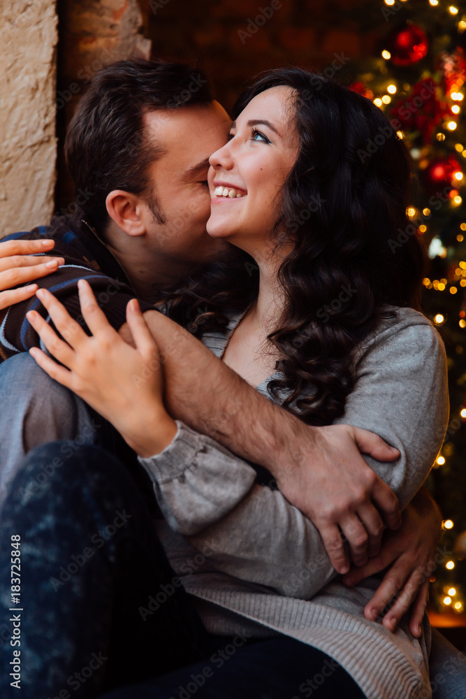 Couple of lovers hugs sitting on the windowsill in the Christmas loft studio. guy is hugging the girl. Couple of lovers hugs sitting on the windowsill in the Christmas loft studio. guy is hugging the girl.