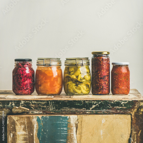 Autumn seasonal pickled or fermented vegetables in jars placed in line over vintage rustic kitchen drawer, white wall background, copy space, square crop. Fall home food preserving or canning photo