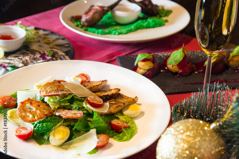 Caesar salad with chicken and parmesan cheese. Christmas or New Year's Eve dinner. Dinner with a Christmas tree. A festive dish for Christmas and New Year with champagne. Christmas tree background Caesar salad with chicken and parmesan cheese. Christmas or New Year's Eve dinner. Dinner with a Christmas tree. A festive dish for Christmas and New Year with champagne. Christmas tree background