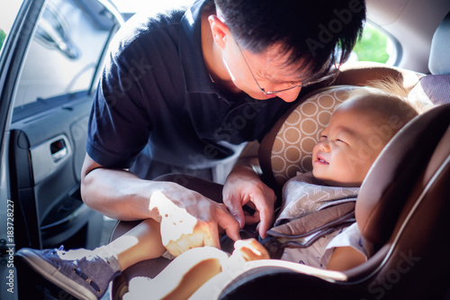 asian father helps his cute little asian 1 year old toddler baby boy child to fasten belt on car seat photo