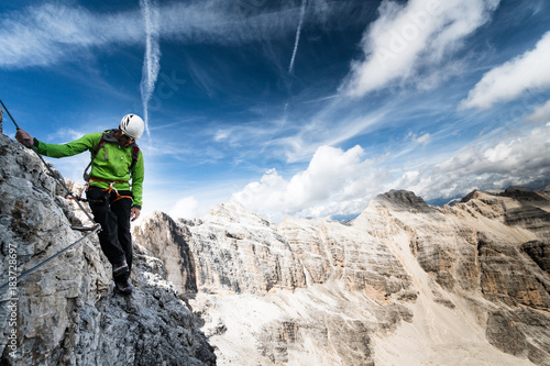 male mountain climber in a green jacket on an exposed Via Ferrata in the Dolomites in Italy with a great view of the surrounding landscape