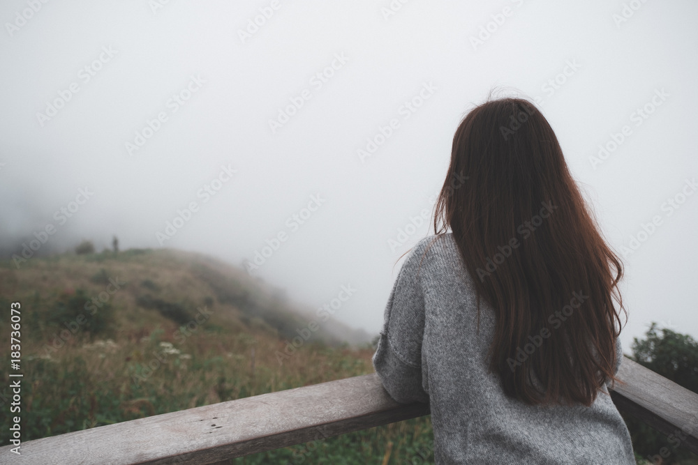 A woman standing alone on balcony looking at white foggy and mountains background