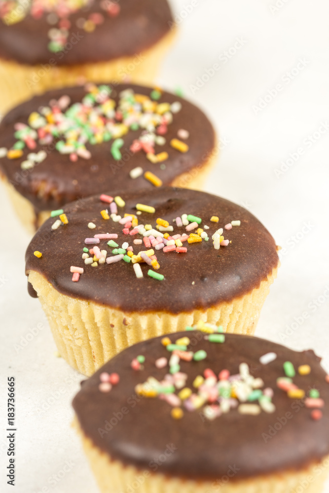 Vanilla cupcakes with chocolate cream and colorful sprinkles isolated on white background