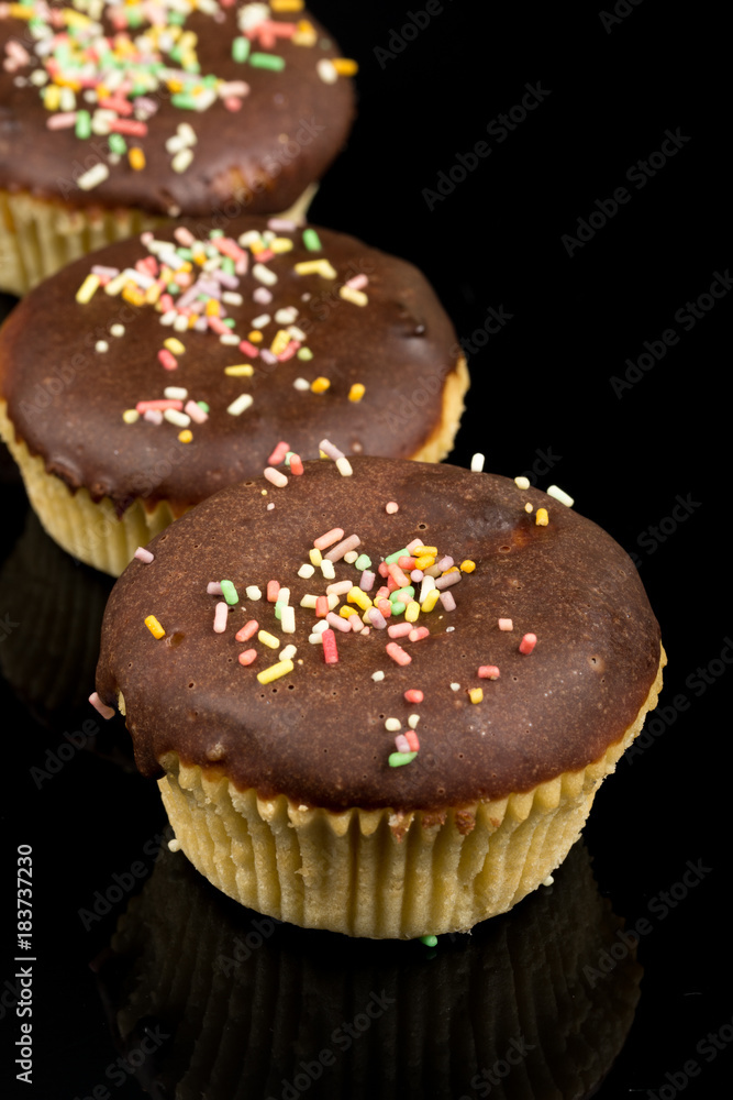 Vanilla cupcakes with chocolate cream and colorful sprinkles above black reflections background
