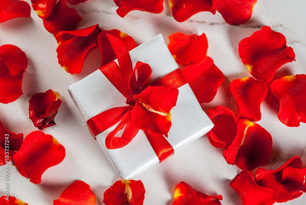 Valentine's day concept, with rose flower petals and white wrapped gift box with red ribbon, on white marble background, copy space top view Valentine's day concept, with rose flower petals and white wrapped gift box with red ribbon, on white marble background, copy space top view