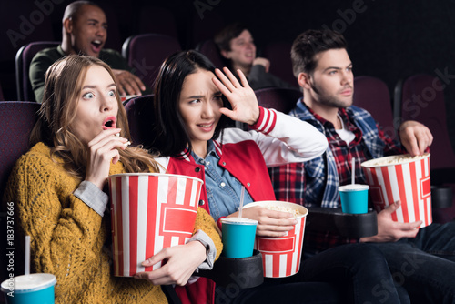 scared friends with popcorn and soda watching horror movie in cinema