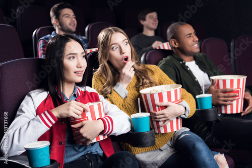 emotional friends with popcorn and soda watching movie in cinema