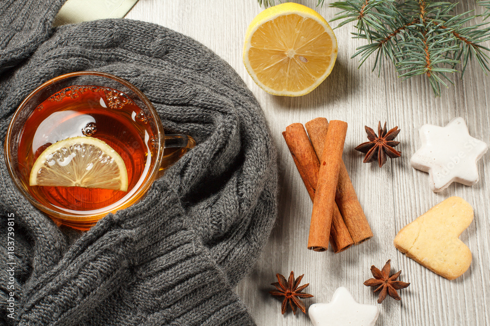 Cup of tea with slice of lemon wrapped up in wool scarf, gingerbread cookies in star and heart shape, natural fir tree branches and spices Cup of tea with slice of lemon wrapped up in wool scarf, gingerbread cookies in star and heart shape, natural fir tree branches and spices