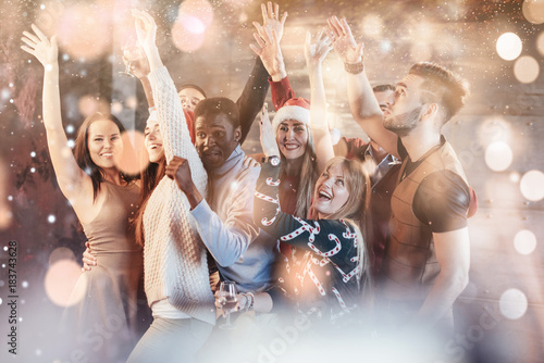 Party with friends. They love Christmas. Group of cheerful young people carrying sparklers and champagne flutes dancing in new year party and looking happy. Bokeh light soft effect