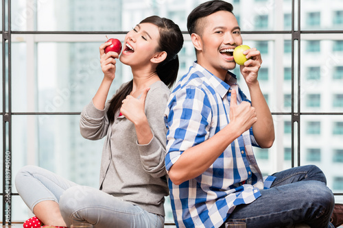 Asian couple  woman and man  having apples as healthy snack in their urban flat
